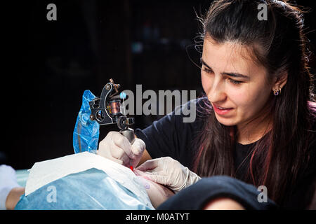 Tatoueur professionnel femme fait un tatouage sur un fémur de jeune fille Banque D'Images