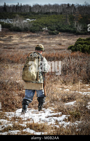 Chasseur Local marche à travers une tourbière herbeux en Sibérie, sous un ciel couvert journée d'automne. La chasse dans la péninsule du Kamtchatka Banque D'Images