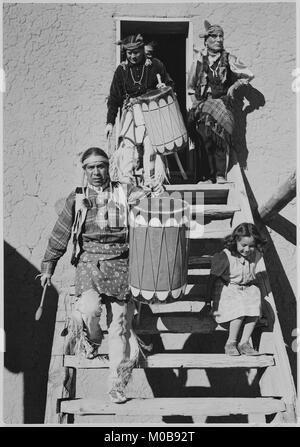 Deux Indiens en ordre décroissant des escaliers en transportant des tambours ; un autre Indien et de l'enfant près de par 'Dance San Ildefonso Pueblo Nouveau Mexique 1942.' (orientation verticale) 1942 Banque D'Images