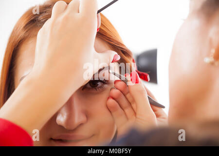 Une jeune femme avec un gland cueille ses red-haired woman's Eyebrows pour atteindre la forme idéale dans un salon de beauté, vue avant Banque D'Images