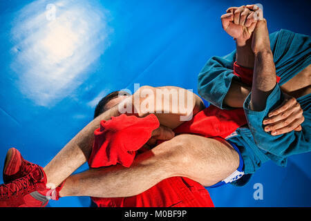 Deux lutteurs de grappling et jiu jitsu dans un kimono bleu et rouge rend armlock sur tatami bleu. Close-up Wrestler lutte de soumission Banque D'Images
