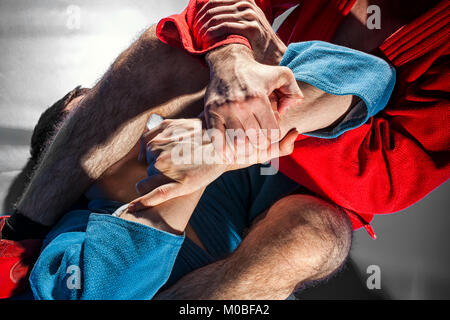 Close-up deux lutteurs de sambo et jiu jitsu dans un kimono bleu et rouge faire . Lutteur de l'homme rend la lutte de soumission ou armbar sur tatami gris Banque D'Images