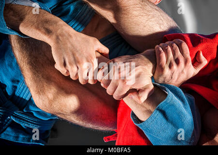 Close-up deux lutteurs de sambo et jiu jitsu dans un kimono bleu et rouge faire . Lutteur de l'homme rend la lutte de soumission ou armbar sur tatami gris Banque D'Images