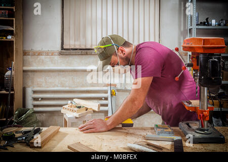 Un jeune homme fort builder carpenter travaille avec un bar en bois pour faire des meubles, des mesures et des coupes dans l'atelier, dans l'arrière-plan de nombreux outils Banque D'Images