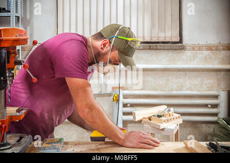 Un jeune homme fort builder carpenter travaille avec un bar en bois pour faire des meubles, des mesures et des coupes dans l'atelier, dans l'arrière-plan de nombreux outils Banque D'Images