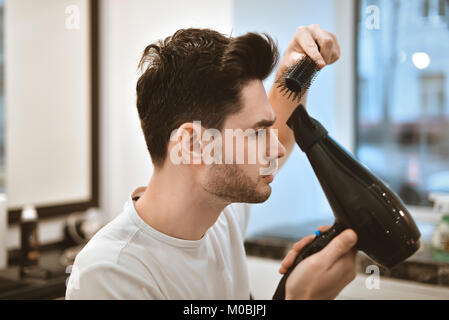 Le gars sécher et fixer ses cheveux. Portrait d'un grand modèle, dans le salon de beauté. Banque D'Images