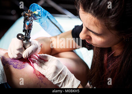 Belle femme brune maître tatouage tatouage faisant d'un petit oiseau avec les peintures rouge machine à écrire pour un tatouage sur la cuisse d'une femme, close-up, vue du dessus Banque D'Images