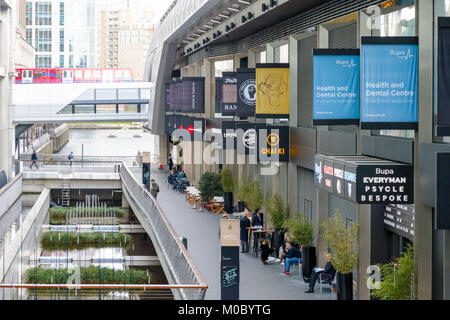 Londres, Royaume-Uni - 25 novembre 2017 - Les restaurants et commerces à traverse Place à Canary Wharf avec les trains DLR passent dans le fond Banque D'Images