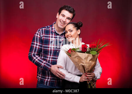 Man embracing sa belle épouse alors qu'elle est titulaire d'un bouquet de roses Banque D'Images