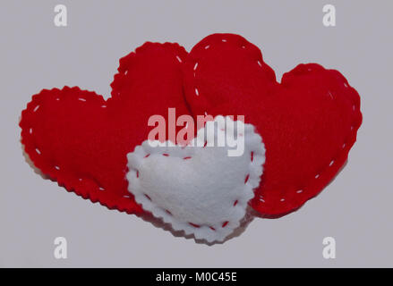 Trois Coeurs en tissu fait main, deux grands rouges avec un petit blanc en face d'eux sur un fond blanc Banque D'Images