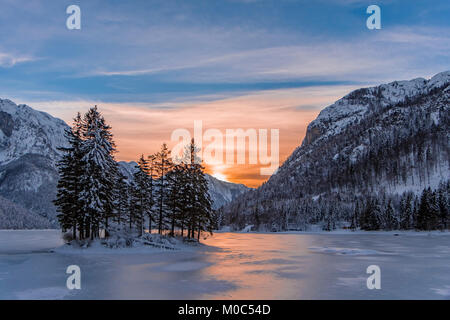 Petite île avec des arbres dans le lac gelé recouvert de neige en hiver Predil wonderland avec beau coucher de soleil Banque D'Images