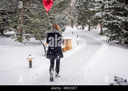 Woman walking in park en hiver tenant un ballon en forme de coeur rouge Banque D'Images