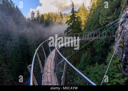 Une vue de dessus du pont suspendu sur un cours d'eau d'une rivière de montagne parmi les vertes forêts de brouillard blanc et des montagnes rocheuses dans un endroit ensoleillé, à l'été Banque D'Images