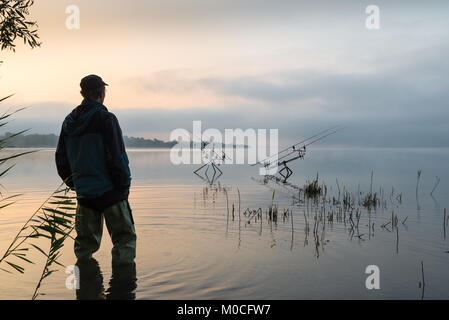 Aventures de pêche, pêche à la carpe. Tôt le matin avec la brume et pêcheur avec des bottes en caoutchouc haute Banque D'Images