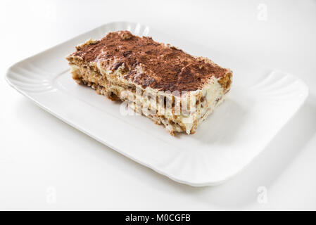 Plaque avec tranche de Tiramisu fait maison, sur fond blanc. Principaux ingrédients : biscuits, crème au mascarpone, poudre de cacao, café, œufs Banque D'Images