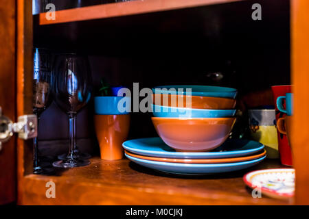 Ouvrir la porte de l'armoire de cuisine en bois armoire avec de nombreux plats colorés, bols, assiettes, tasses, verres sur des étagères closeup Banque D'Images