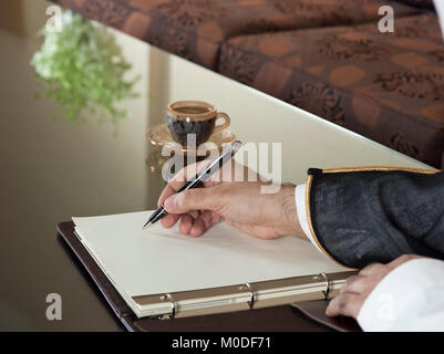 L'homme de l'Arabie saoudite écrit à la main sur un ordinateur portable dans un environnement d'accueil de luxe, le port d'Arabie Thob, Ghutra Bisht noir et Banque D'Images