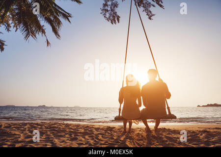 Couple amoureux romantique assis ensemble à corde balançoire à sunset beach, silhouettes de jeune homme et femme en vacances ou voyage de noces Banque D'Images