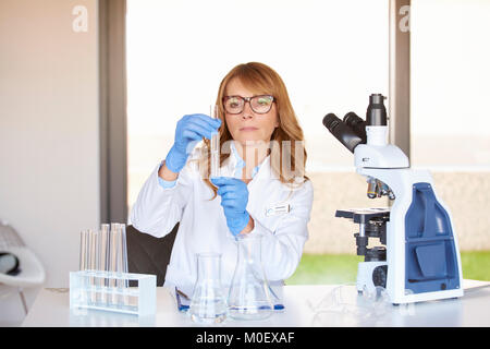 Female doctor holding hand cube test assis à côté de son bureau et l'analyse au microscope les résultats des tests médicaux. Banque D'Images