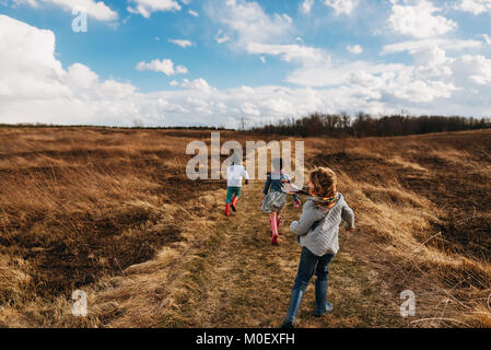 Trois enfants courir le long d'un sentier dans un paysage rural Banque D'Images