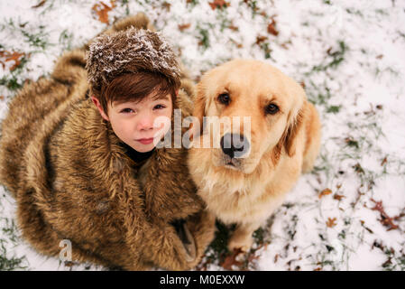 Golden retriever dog et garçon enveloppé dans une couverture assis dans la neige Banque D'Images