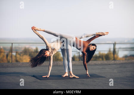 Deux belles femmes faisant du yoga asana Ardha Chandrasana sur le toit à l'extérieur. Poser la demi-lune. Banque D'Images