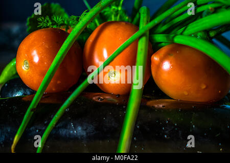 Les tomates rouges frais avec l'oignon vert feuilles conservées sur les aubergines et gouttes d'eau sur eux
