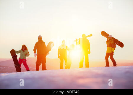 Groupe d'amis sérieux avec ski et snowboards contre coucher du soleil Banque D'Images