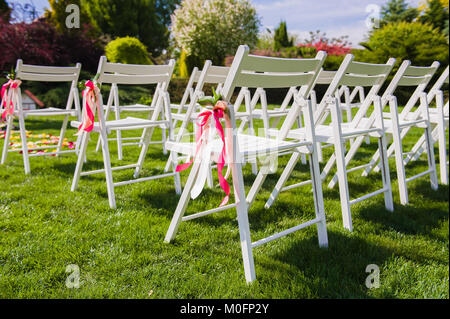 Détail de la décoration de mariage avec de longues bandes lumineuses attachées sur les sièges à l'extérieur. Se concentrer sur les couleurs rose et pêche à rubans pour chaises blanc Banque D'Images