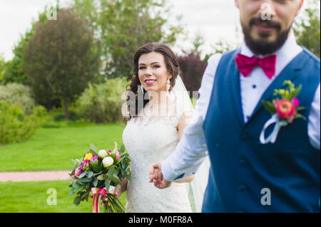 Marié avec une barbe tenant de sa main smiling happy mariée en dentelle robe blanche avec détails rose - bouquet de pivoines, buotoniere et attachez-bow Banque D'Images