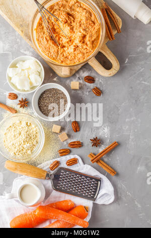 Cuisson saine de gâteau aux carottes, dessert végétalien Ingrédients : Pâte dans un bol, Chia, noix de coco, lait d'amande, beurre de noix. Pain de carottes, fond gris. Banque D'Images