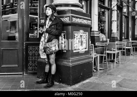 Photographie de rue en noir et blanc à Londres : jeune femme sur téléphone mobile à Leadenhall Market, City of London. Banque D'Images