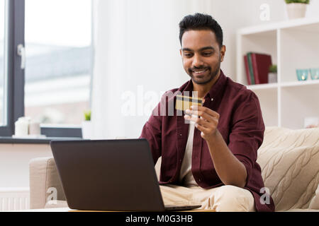 Smiling man with laptop and credit card at home Banque D'Images