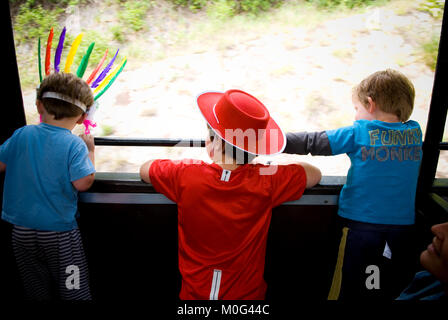 Capture d'arrière de trois jeunes garçons, âgés entre deux déguisé en indien et un cowboy, à la fenêtre de sortie du train en mouvement dans les Cévennes, France Banque D'Images