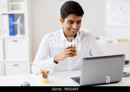 Businessman with laptop drinking coffee at office Banque D'Images