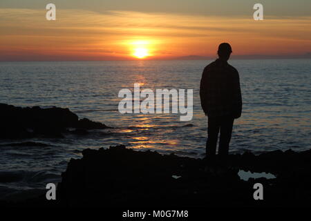 Un homme devant un coucher du soleil à Laguna Beach. Le soleil se couche sur l'océan comme un jeune homme montres qu'elle. Banque D'Images