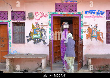 CHITTORGARH, Rajasthan, INDE - Le 14 décembre 2017 : une maison traditionnelle avec des peintures colorées et une femme portant sur la tête de l'eau pot Banque D'Images