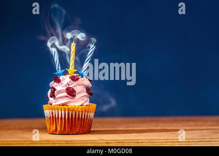 Birthday cupcake avec trois bougies soufflées sur le dessus sur fond bleu profond dans un nuage de fumée un Banque D'Images