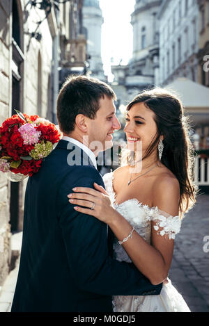 Jeunes mariés heureux étreindre. Utilisable en extérieur. Belle brune mariée est maintenant le mariage bouquet de fleurs rouges et roses. Banque D'Images