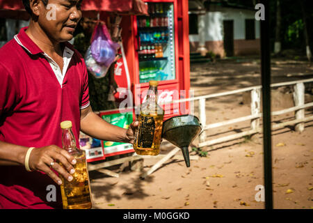 Tuk Tuk driver du remplissage du réservoir de carburant de l'ancienne bouteille de whisky bourbon, Angkor Thom, au Cambodge. Banque D'Images