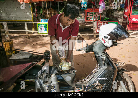 Tuk Tuk driver du remplissage du réservoir de carburant de l'ancienne bouteille de whisky bourbon, Angkor Thom, au Cambodge. Banque D'Images