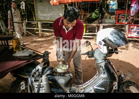 Tuk Tuk driver du remplissage du réservoir de carburant de l'ancienne bouteille de whisky bourbon, Angkor Thom, au Cambodge. Banque D'Images