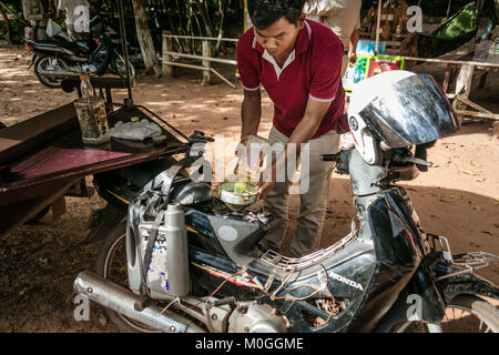 Tuk Tuk driver du remplissage du réservoir de carburant de l'ancienne bouteille de whisky bourbon, Angkor Thom, au Cambodge. Banque D'Images