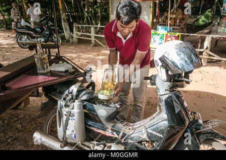 Tuk Tuk driver du remplissage du réservoir de carburant de l'ancienne bouteille de whisky bourbon, Angkor Thom, au Cambodge. Banque D'Images