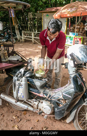 Tuk Tuk driver du remplissage du réservoir de carburant de l'ancienne bouteille de whisky bourbon, Angkor Thom, au Cambodge. Banque D'Images