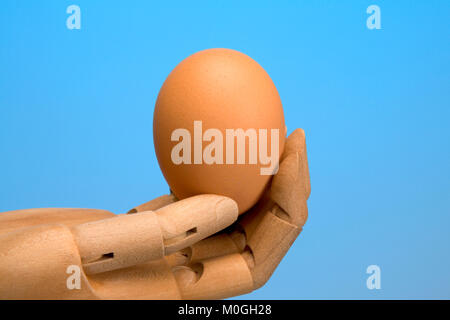 Main mannequin artistes offrant un seul œuf, fond bleu clair Banque D'Images