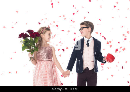 Adorable enfants heureux avec des roses en forme de cœur et boîte-cadeau tenant la main et en souriant l'un l'autre on white Banque D'Images