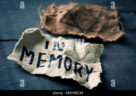 Libre d'un insigne et un juif déchiqueté feuille de papier jaunâtre avec le texte en mémoire écrit en C, sur une surface en bois rustique gris Banque D'Images