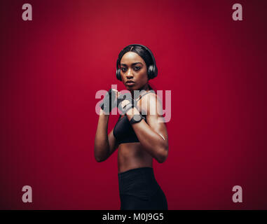 Jeune femme africaine boxing posant en position de combat à la recherche à l'appareil photo. Fit young female boxer avec un casque prêt pour combattre sur bac rouge Banque D'Images