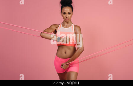 À l'aide d'une femme dure resistance band dans sa routine d'exercice. L'exercice de l'athlète féminine avec bande de résistance contre fond rose. Banque D'Images